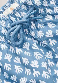 Bañador azul con un patrón de coral blanco, confeccionado con tela ligera, con cintura de cordón y detalles de herrajes en contraste.