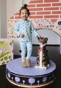 Light blue, ribbed pajama set with small blue patterns, paired with beige slip-on shoes. Child stands on a textured, round purple surface next to a painted tiger statue.