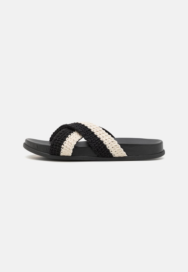 Sandale à glissière noire avec semelle épaisse et deux brides croisées en tricot noir et blanc cassé.