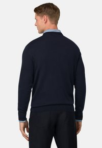 Suéter de punto azul marino con mangas largas y cuello redondo, presenta puños y dobladillo acanalados. Se puede ver un cuello de camisa azul claro debajo.
