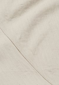 Tissu beige avec couture diagonale visible et texture fine côtelée en gros plan.