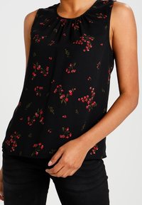 Svart ärmlös topp med en rynkad halsringning, prydd med ett blommönster i röd och grön, tillverkad av lättviktig tyg.