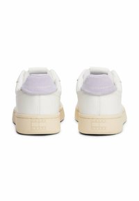 Witte leren sneakers met een lichtpaarse suède hieltab, een crème rubberen zool en geëmbossiseerde "TOMMY JEANS" branding op de hiel.