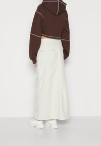 Brown cropped hoodie with light gray stitching, paired with a long, cream cargo skirt featuring side pockets and a relaxed fit. White sneakers.
