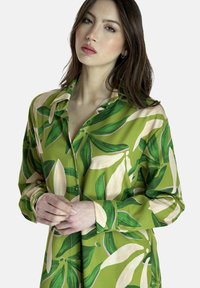 Camicia verde a maniche lunghe con un motivo floreale caratterizzato da grandi foglie e petali color crema. Tessuto morbido con chiusura a bottoni e colletto.