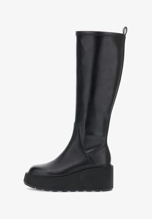 Bota alta de piel negra con plataforma y suela gruesa, con una lengüeta en la parte posterior, mostrada en vista lateral sobre un fondo blanco.