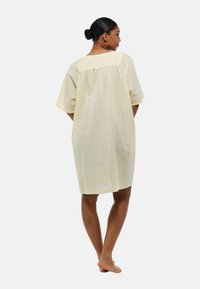 Nuisette légère en coton rayé jaune et blanc avec des manches courtes et une coupe ample, dotée d'un dos froncé pour plus de facilité de mouvement.