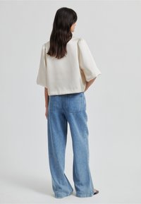 Krémová halenka s krátkým rukávem a mírně volným střihem, v kombinaci se světle modrými širokými džínami s kapsami na zadní straně.