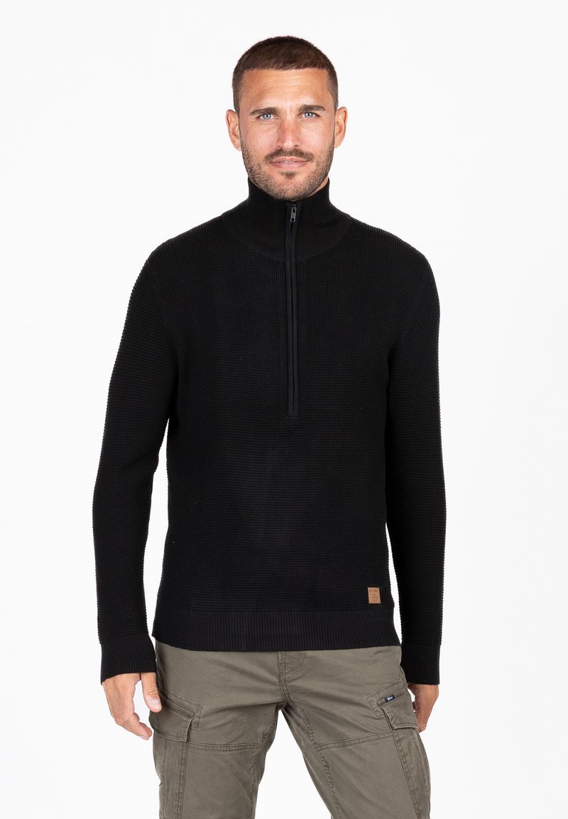 Maglione nero in maglia con colletto alto e mezza cerniera. Presenta polsini e orlo a coste, con un piccolo etichetta marrone in basso a sinistra.