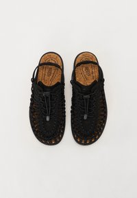 Sandales tressées noires avec semelle en liège et lacets ajustables. Design ouvert et semelles en caoutchouc, avec une surface texturée et des brides respirantes.