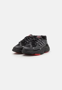 Black athletic shoes with mesh panels, thick soles, and red accents. Features lace-up closure and textured rubber outsoles.