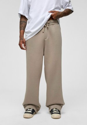 Beige sweatpants with elastic waistband, drawstring, and side pockets, styled with a loose-fitting white t-shirt and black sneakers.