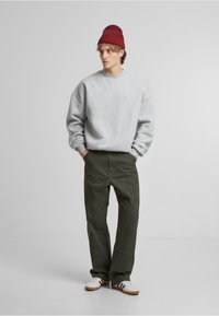 Grå crewneck sweatshirt, olivengrønne bukser med lommer og hvide sneakers med røde og brune striber, toppet med en rød strikket hue.