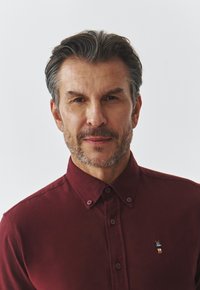 Bordeaux button-up skjorte med en blød tekstur, der har et lille broderet logo på venstre bryst og en klassisk krave.