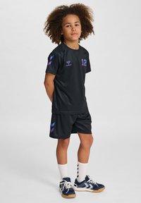 Zwart sportuniform met paarse accenten. Korte mouwen shirt en bijpassende shorts, met het nummer 12. Draagt witte sokken en blauwe schoenen.