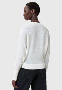 Valkoinen, kevyt neulepaita, jossa ribbireunat hihansuissa ja helmassa, rento istuvuus ja raglan-hihat. Raskasta neulosta hienovaraisella kiillolla.