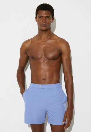 Lyseblå badeshorts med en glat tekstur, der har sidelommer og en sølvfarvet knapdetalje på linningen.