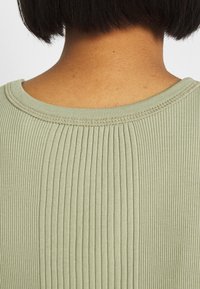 Jasnozielony prążkowany top z okrągłym dekoltem, ściśle rozmieszczonymi pionowymi paskami i subtelną fakturą dzianiny.