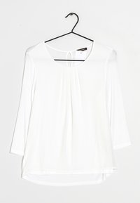 Haut à manches longues blanc avec un col rond, un détail plissé à l'avant, un ourlet arrondi et une petite ouverture en forme de clé au dos. Fait en tissu léger.