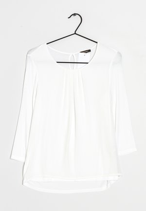 Hvid langærmet top med rund halsudskæring, plisseret detaljer foran, buet kant og et lille nøglerumsåbning bagpå. Fremstillet af letvægtigt stof.
