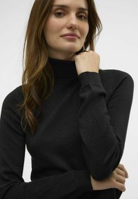 Maglione a dolcevita nero realizzato in tessuto a costine. Presenta maniche lunghe e un design aderente con una leggera lucentezza. Collo alto.