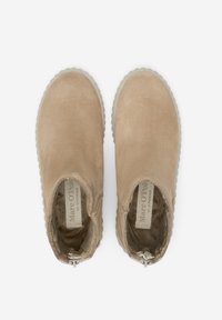 Bottines en suède beige à bout rond et panneaux élastiques sur les côtés. Semelle en caoutchouc blanche avec un bord festonné. Intérieur doublé d'un matériau doux.