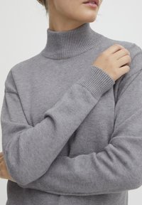 Maglione a collo alto grigio chiaro realizzato in morbido materiale a maglia, con polsini e colletto a coste, dalla vestibilità rilassata e maniche lunghe.
