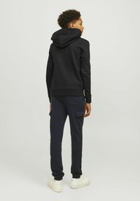 Črna kapuca s kenguru žepom, v kombinaciji z mornarsko modrimi cargo hlačami z stranskimi žepi in belimi športnimi copati.