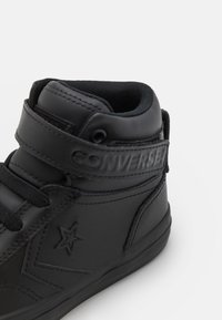 Czarne, wysokie trampki wykonane z syntetycznej skóry, z wyściełanym kołnierzem, sznurowanym przodem, zapięciem na rzep oraz wytłoczonym detalem z logo.