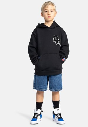 Sweat à capuche noir avec un logo blanc, shorts en denim, baskets noires et bleues, et chaussettes noires. Style décontracté, coupe ample avec une poche avant.