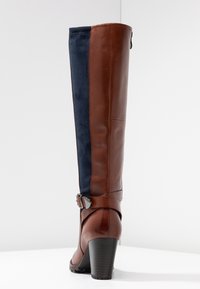 Bota alta de cuero marrón y ante azul marino con tacón grueso, detalle de hebilla en el tobillo y un acabado suave.
