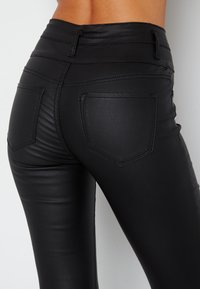 Pantalon en similicuir noir avec une texture lisse, doté de deux poches arrière et de détails de couture subtils sur une coupe ajustée.