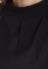 Černá strukturovaná tkanina s jemným leskem, vybavená kulatým výstřihem a centrálním skladem v oblasti hrudníku.