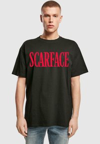 Svart bomull T-skjorte med et stort rødt "SCARFACE" grafikk foran. Korte ermer og rund hals. Løs passform.