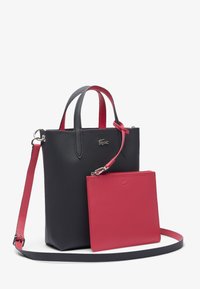 Sac fourre-tout en cuir noir texturé avec de courtes poignées et une pochette rose détachable. Présente un accent de logo argenté et une longue bandoulière réglable.