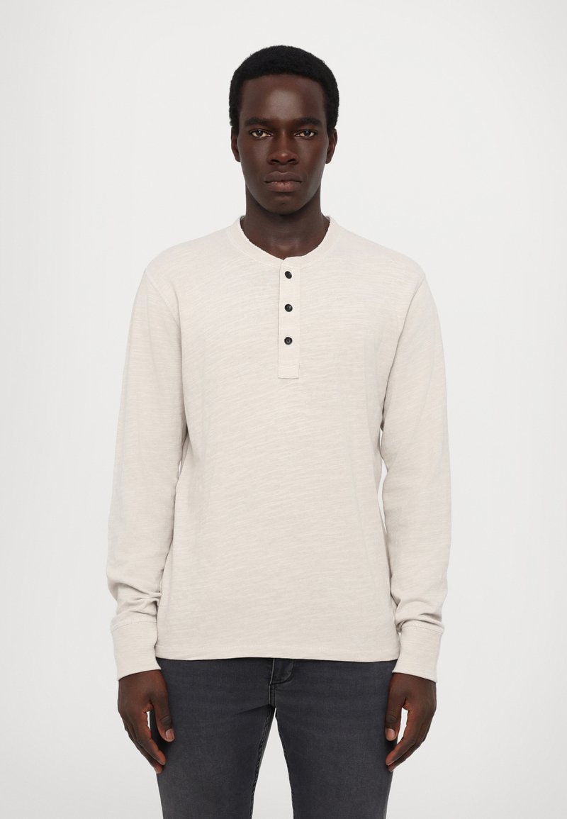 Langermet henley-skjorte i lys beige, laget av teksturert stoff med rund hals, tre svarte knapper og tettsittende mansjetter.