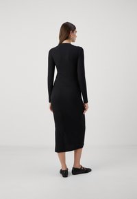 Μαύρο ριγωτό μίντι φόρεμα με μακριά μανίκια, εφαρμοστή γραμμή και ίσια κάτω πλευρά. Φορεμένο με μαύρες επίπεδες παπούτσια, ελάχιστες λεπτομέρειες και λείες υφές.