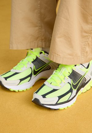 Neonově zelené a černé běžecké boty z prodyšného materiálu, s kontrastními překryvy a texturovanými podrážkami, zdobené světlými tkaničkami a polstrovaným designem.