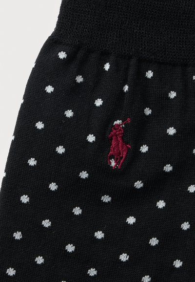 Tissu noir à pois blancs avec un petit logo brodé de joueur de polo rouge près du centre.