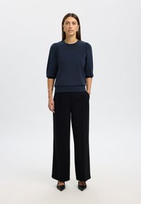 Granatowy pulower z bufiastymi rękawami, zestawiony z czarnymi szerokimi spodniami i czarnymi szpiczastymi szpilkami. Gładka tkanina, minimalistyczny design.