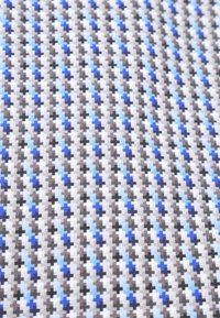 Textiel met een geometrisch patroon van blauwe, grijze en zwarte kruizen op een witte achtergrond, met een gladde, geweven textuur.