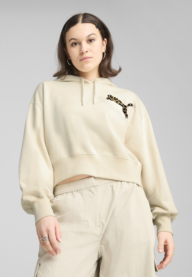Beige cropped hoodie met een koord in de capuchon, voorzien van een geborduurd logo met luipaardprint op de linkerborst. Zachte textuur; relaxte pasvorm.