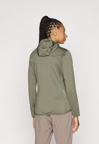 Chaqueta ligera de color verde oliva con un diseño ajustado, capucha y mangas largas. Tejido texturizado y detalle de bolsillo lateral.