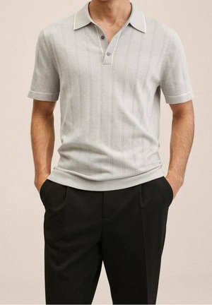 Hellgraues Polohemd aus Strick mit geripptem Muster, kurzen Ärmeln und einem Kragen mit zwei Knöpfen. Kombiniert mit schwarzen Hosen.