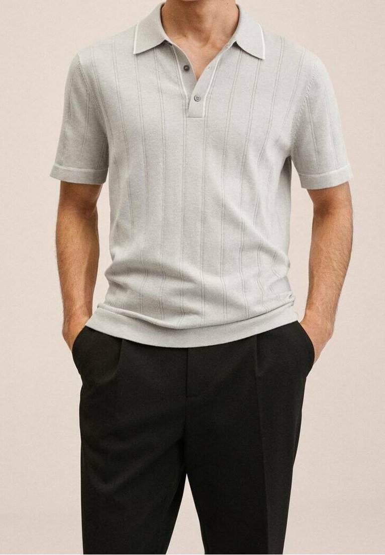 Polo en maille gris clair avec une texture côtelée, manches courtes et col à deux boutons. Associé à un pantalon noir.