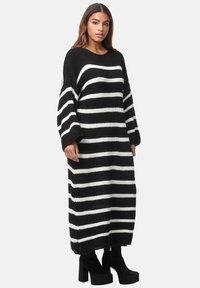 Schwarz-weiße gestreifte Strickkleid, langärmlig, lockere Passform, strukturiertes Material, bis zur Mitte der Wade reichend, kombiniert mit schwarzen Plateau-Stiefeln.