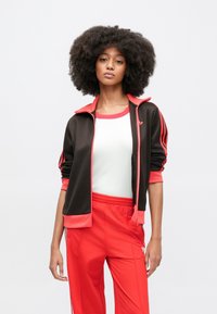 Mustast ja punasest sportlikust jope eest lukuga, soonikkoega kraega ja varrukatel kolme triibuga, kombineeritud punaste pükste ja valge särgiga.