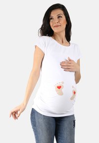 Weißes Umstandsshirt mit kurzen Ärmeln, das im Bauchbereich bedruckte Babyfüße mit roten Herzen zeigt. Aus weichem, dehnbarem Stoff.