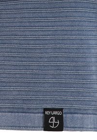 Tejido a rayas en tonos de azul, con un patrón texturizado. Incluye una etiqueta negra con texto blanco "KEY LARGO" y el logo en el borde inferior.