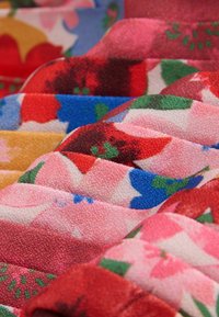Színes szövet virágmintákkal piros, rózsaszín, kék és sárga árnyalatokban. Puha tapintású, kiemelkedő, steppelt mintázattal és változatos színátmenetekkel.